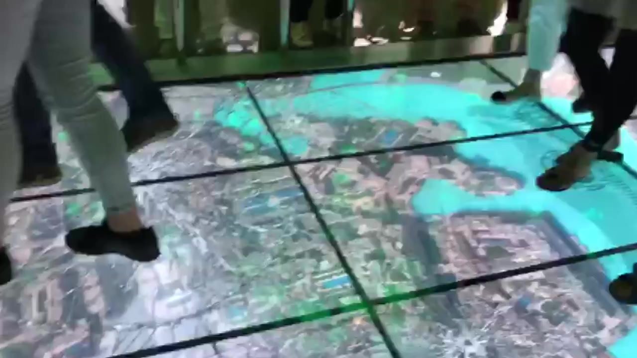 People walking on a large interactive LED floor at Burj Khalifa, displaying a high-resolution digital aerial map of Dubai with interactive light triggers.